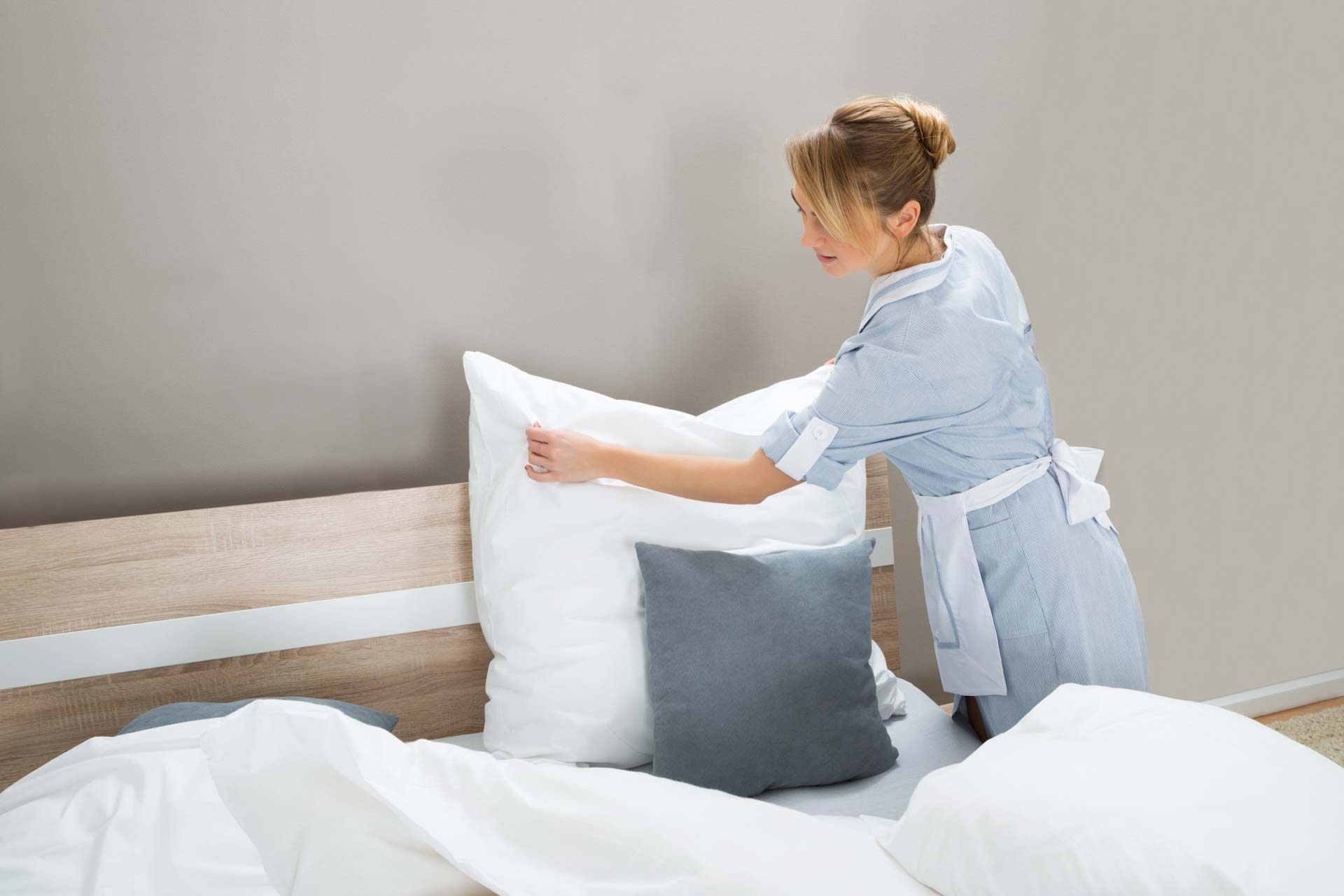 Person making a bed with white and gray pillows in a bedroom setting.