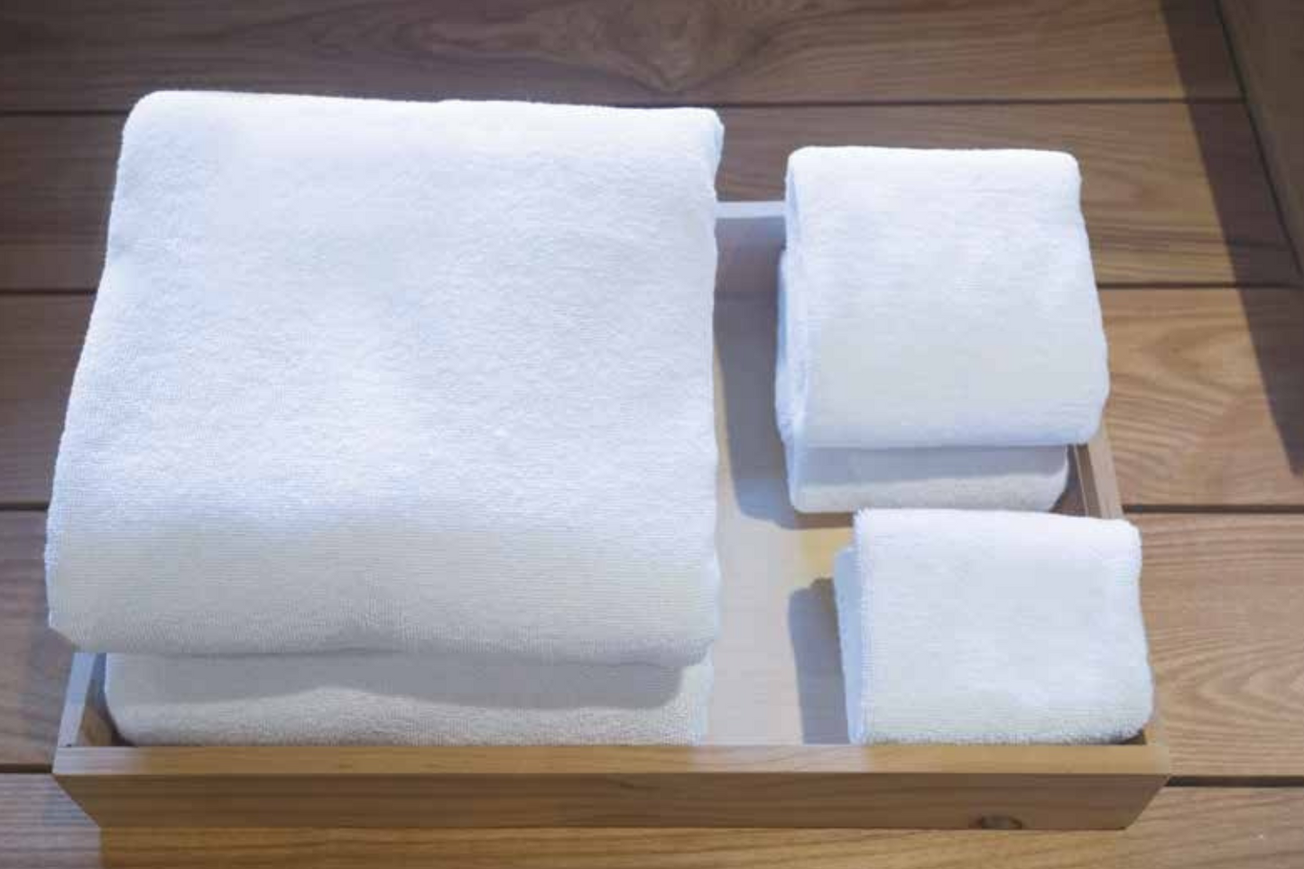 Stack of white towels on a wooden tray with a wooden surface background