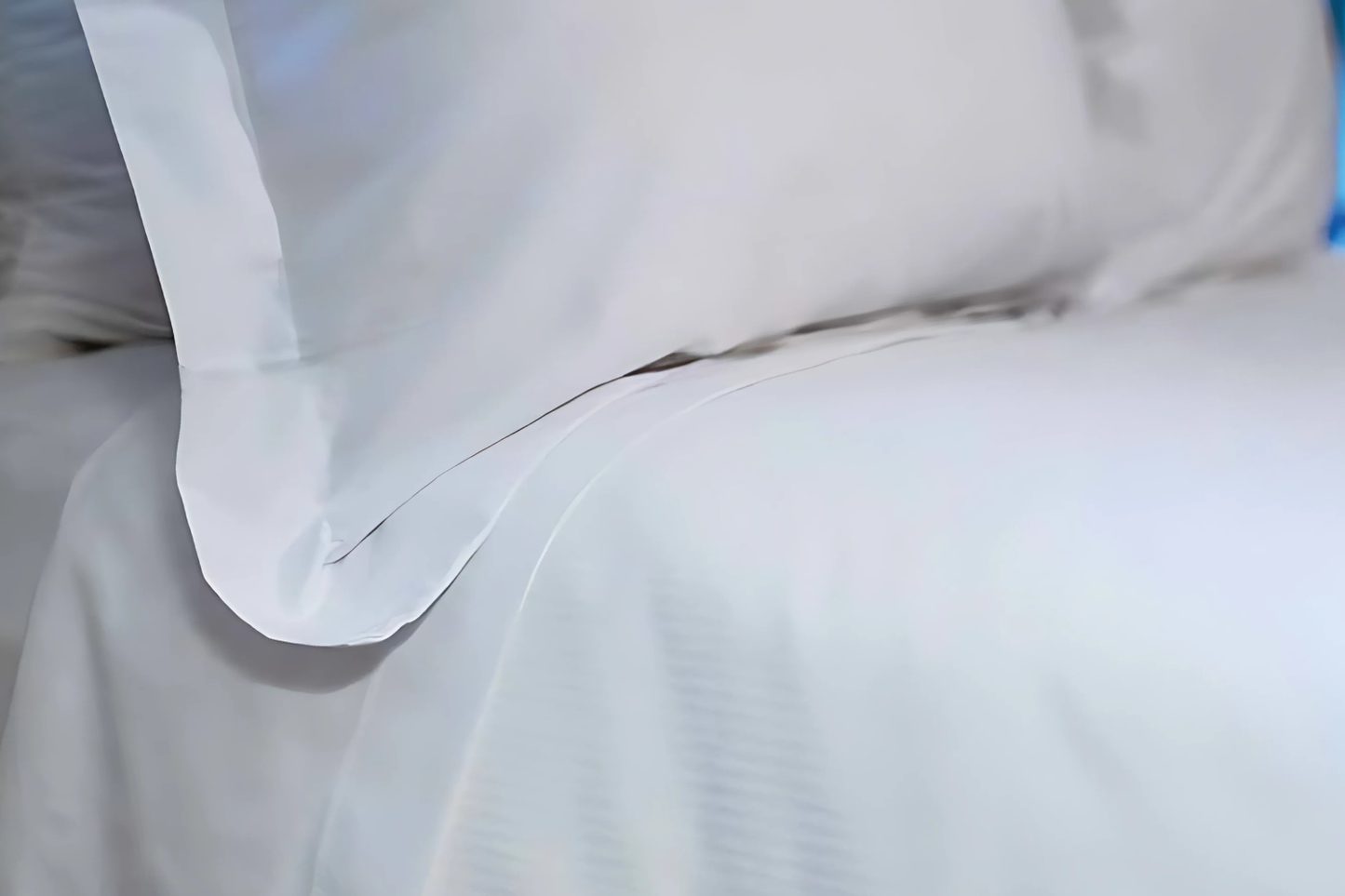 Close-up of white bedding with a pillow on a bed.