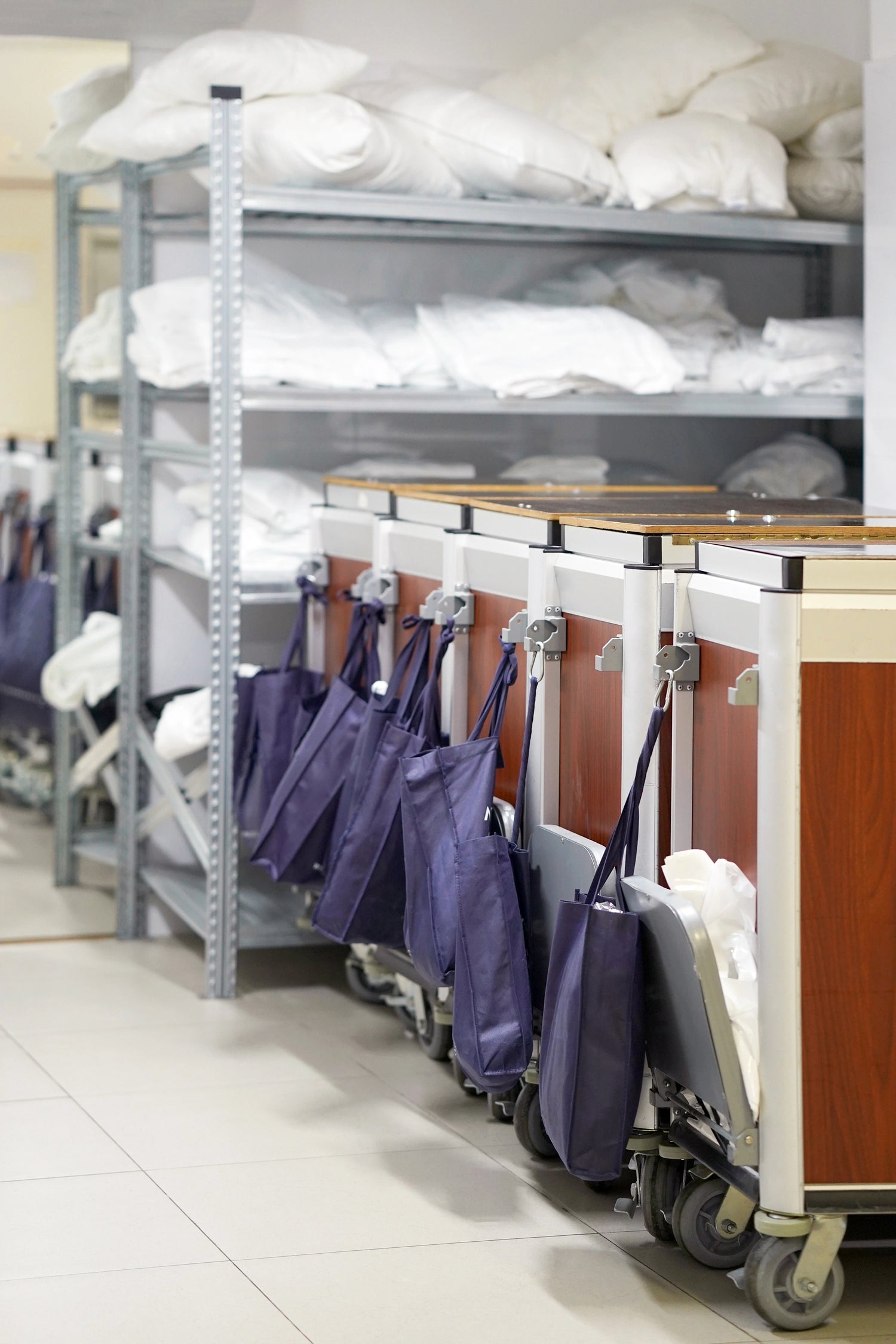 Storage room with shelves filled with white pillows and a row of purple bags on carts.