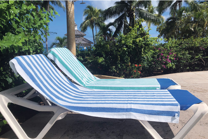 Two lounge chairs with blue and white striped towels on a sunny day with palm trees in the background.