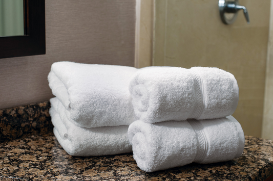 Stack of white towels on a granite countertop with a mirror and faucet in the background.