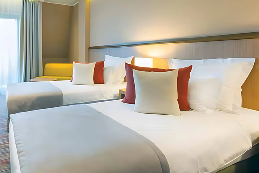 Two neatly made beds with white bedding and colorful pillows in a well-lit room.