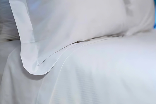Close-up of white bedding with a pillow on a bed.