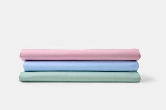 Stack of three folded fabrics in pink, blue, and green on a white background