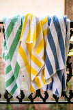 Green, yellow and blue island stripe pool towels hung over a railing. Thomaston Mills Towels.