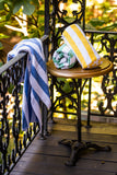 Blue island stripe pool towel hung over a railing with yellow and green island stripe pool towels rolled on a table. Thomaston Mills Towels.