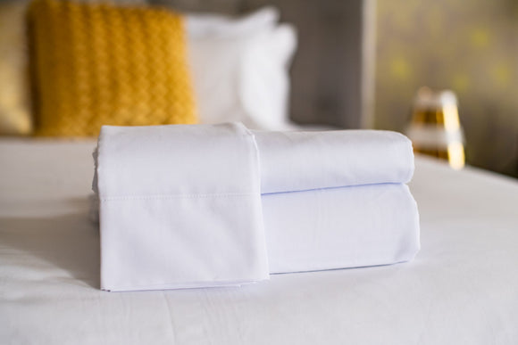 Thomaston T-250 Royal Suite pillowcase laid over folded sheets laying on a bed made with Thomaston T-250 Royal Suite sheets and pillowcases.