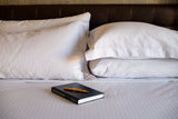 Bed made with Thomaston Mills T-310 Satin Stripe Sheets and Pillowcases with a book and pen laying on the bed..
